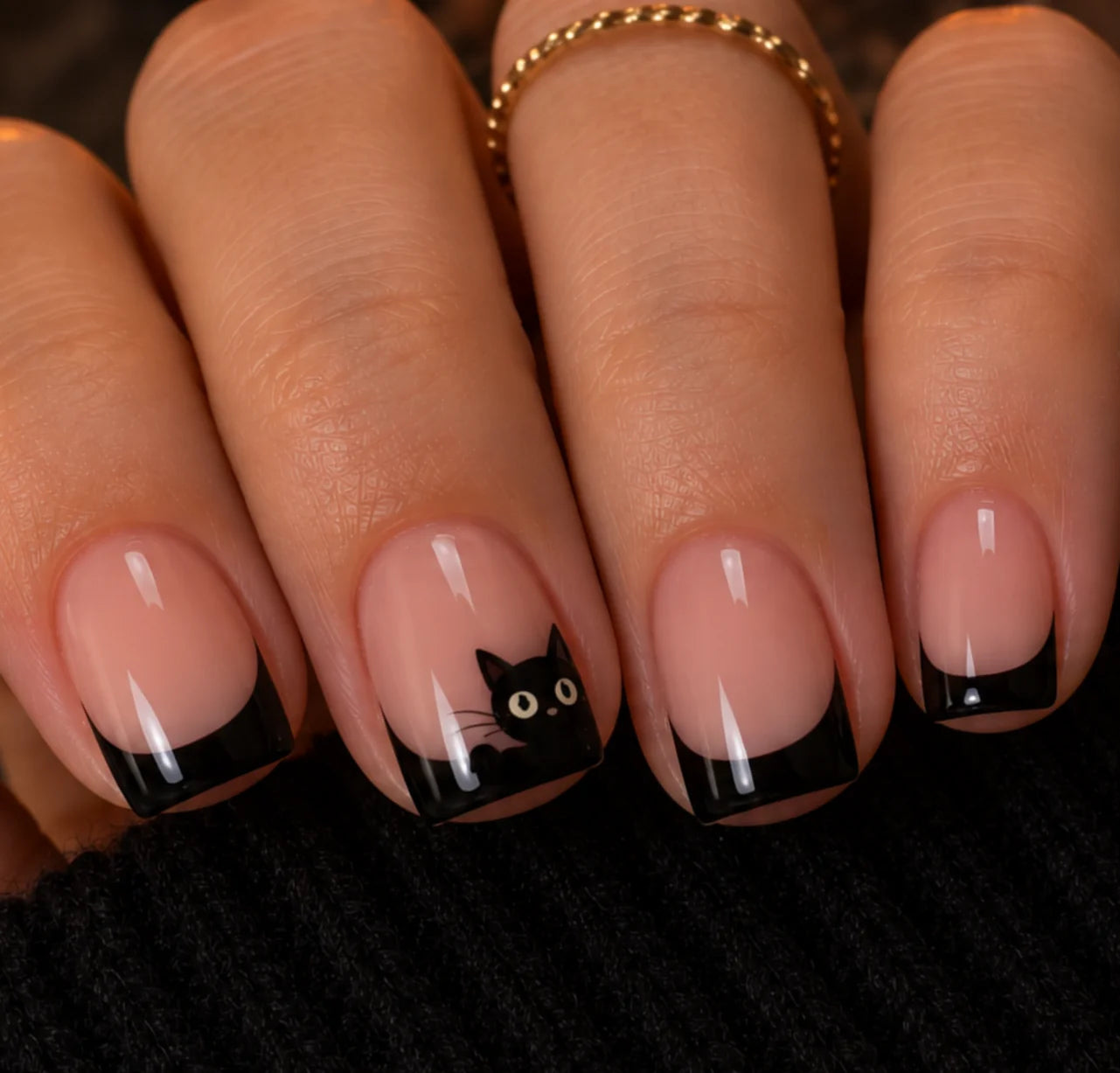 Skinny black French tip nails with a tiny black cat peeking over the ring finger